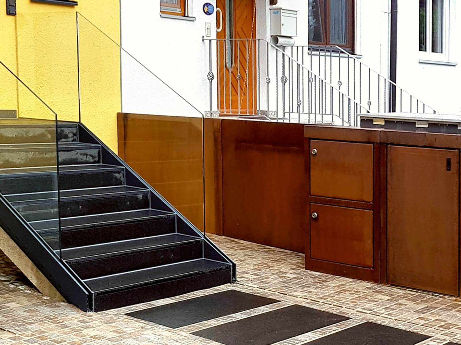 Sicht auf Haustür mit Glastreppe und Paketbriefkasten aus Cortenstahl