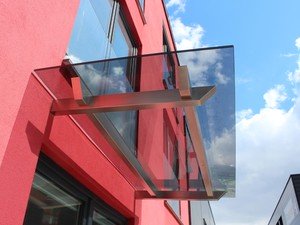 Glasvordach mit Balkenträgern aus Edelstahl in markantem Design