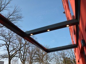 Großes Glasvordach mit umlaufendem Stahlrahmen in schwarz und integrierten Spots