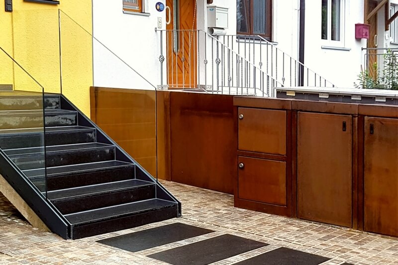 Mehrere Paketboxen aus Cortenstahl nebeneinander vor modernem Hauseingang